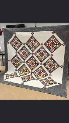 a woman standing next to a large quilt on the floor in front of a table