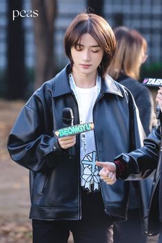 a young man in a black leather jacket holding a microphone and looking at his cell phone