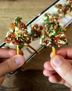 two hands holding tiny trees made out of food on toothpicks with toppings