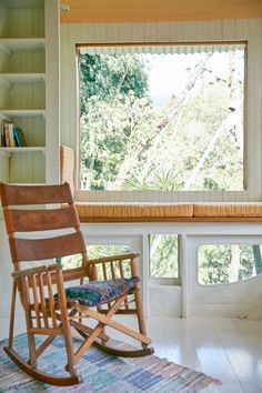 a rocking chair sitting in front of a window next to a book shelf and bookshelf