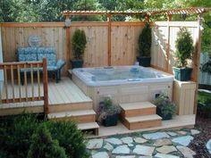 a hot tub sitting in the middle of a garden next to a wooden fence and steps