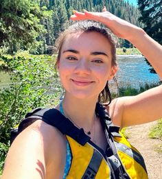 a woman standing in front of a lake wearing a life jacket and holding her hand up to her head