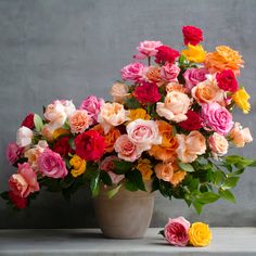 a vase filled with lots of different colored flowers on top of a white table next to a gray wall