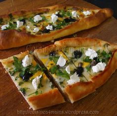 two slices of pizza with cheese, olives and herbs on them sitting on a cutting board