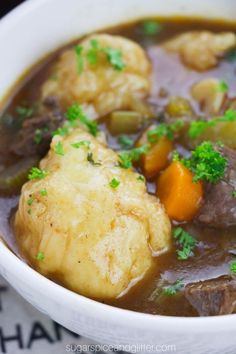 a white bowl filled with beef and dumplings on top of a table next to a napkin