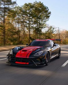 a red and black sports car driving down the road with trees in the back ground