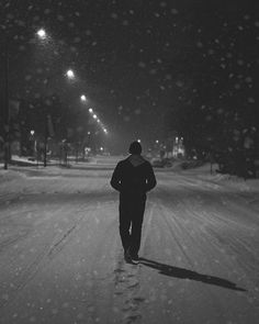 a man walking down a snow covered road at night with street lights in the background