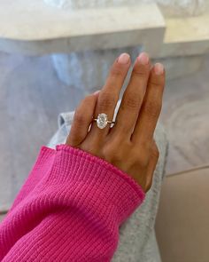 a woman's hand with a diamond ring on top of her left hand, wearing a pink sweater