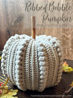 a crocheted pumpkin sitting on top of a table next to leaves and a wooden stick