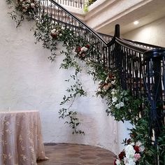 an indoor staircase with flowers and greenery on the railing, next to a table