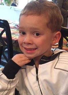 a little boy that is sitting down with a smile on his face and looking at the camera