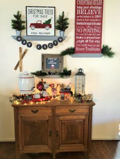 christmas decorations on top of a wooden cabinet in a room with two framed signs above it