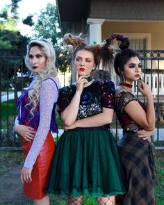 three women dressed in costumes standing next to each other near a fence and gated area