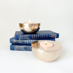 three books stacked on top of each other next to a silver bowl with a candle in it