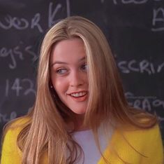 a woman with long blonde hair standing in front of a chalkboard and smiling at the camera