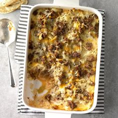 a casserole dish with meat and cheese in it on a striped towel next to a spoon