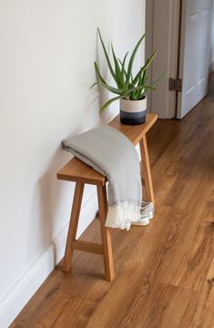 a wooden bench with a blanket on it and a potted plant next to it