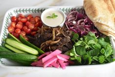 a white tray topped with meat, veggies and pita bread