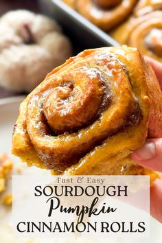 someone holding up a cinnamon roll with the words fast and easy sourdough pumpkin cinnamon rolls