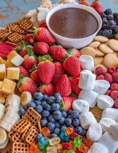 a platter filled with fruit, crackers, and other snacks next to a bowl of chocolate