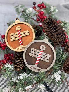 two wooden christmas ornaments sitting on top of pine cones and evergreen branches with red and white striped candy canes