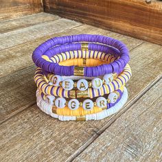 "Purple and Gold Bracelet Stack - Perfect to pair with your game day attire! Mix and Match! Wear one or wear them all together! Matching earrings: https://ellebellehandmade.etsy.com/listing/1598940389 Please Note: When putting the bracelet on please \"roll\" it on. Stretching out the bracelet can cause it to change size over time. Bracelets are 7\" in length. If a different size is needed please let me know." Lsu Game Day, Gold Bracelet Stack, Lsu Game, Gold Bracelets Stacked, Clay Bead Bracelet, Handmade Jewelry Bracelets, Clay Bracelet, Gold Cross Necklace, Gold Bead Bracelets