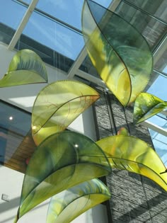 an artistic glass sculpture in front of a building with large leaves hanging from it's sides