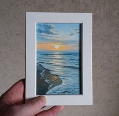 a person holding up a painting in front of a wall with the sun going down