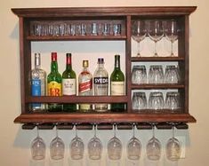 wine glasses and liquor bottles are lined up on a wooden shelf with shelves below them