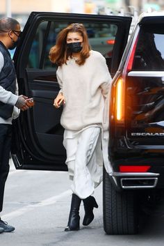 a woman wearing a face mask walking out of a car with another man in the background