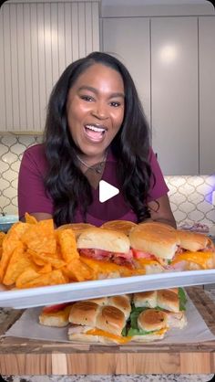 a woman sitting in front of a tray filled with sandwiches and chips