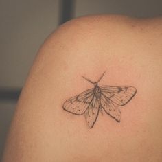 a small moth tattoo on the back of a woman's shoulder