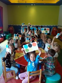 a group of children sitting around a table holding up paper cutouts with dots on them