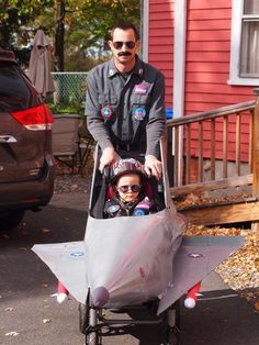 a man pushing a child in a small airplane shaped vehicle with another person behind him