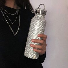 a woman wearing a black shirt holding a silver bottle in her right hand and a necklace on her left arm