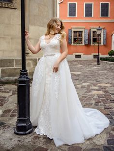 a woman standing next to a lamp post in front of an orange building wearing a wedding dress