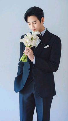 a man in a tuxedo holding flowers and looking down at his suit jacket