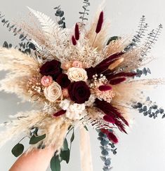 an arrangement of dried flowers and feathers in someone's hand on a white wall