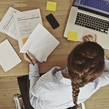 a woman sitting at a desk with papers and laptop computer on it, looking down