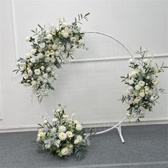 two wreaths with white flowers and greenery on the floor in front of a wall