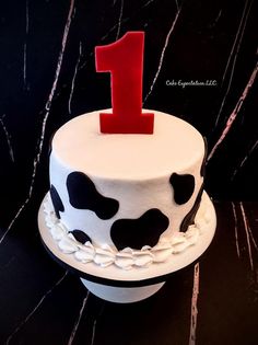 a birthday cake decorated with black and white cow print, red number one on top