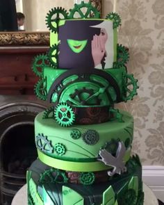 a multi layer cake with green frosting and gears on the top, sitting in front of a fireplace