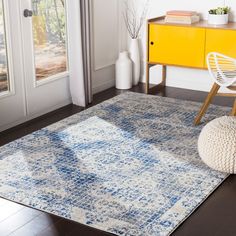 a blue and white area rug on the floor in front of a yellow cabinet next to a window