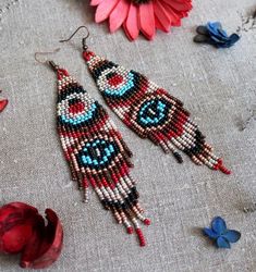 two red and blue beaded earrings sitting on top of a table next to flowers