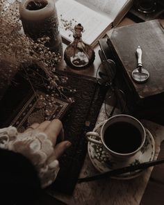 a person holding a cup of coffee next to an open book and other items on a table