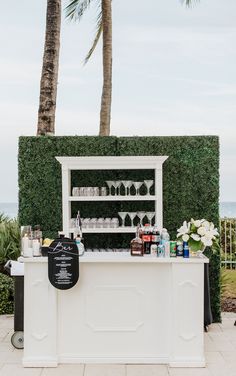 an outdoor bar with wine glasses and bottles on it next to the ocean in front of some palm trees