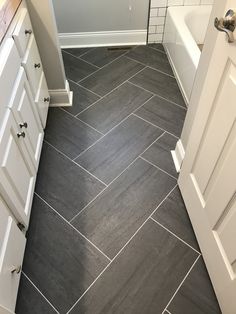 a bathroom with gray tile flooring and white cabinetry next to the bathtub