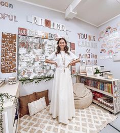 a woman standing in front of a white wall with lots of pictures on the walls