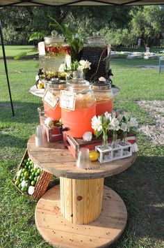 there is a table with drinks on it in the grass and some flowers are around