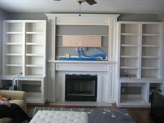 a living room with white bookcases and a man sitting on a couch in front of a fireplace